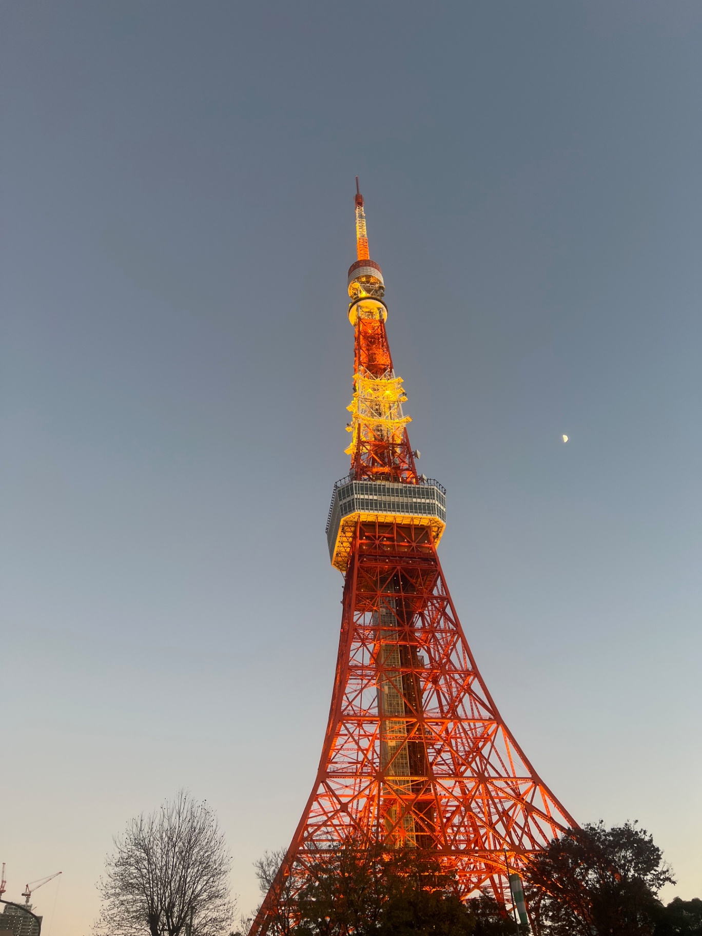 Tokyo — Tokyo Tower glowing orange against deep dusk, a thin moon hanging beside it.