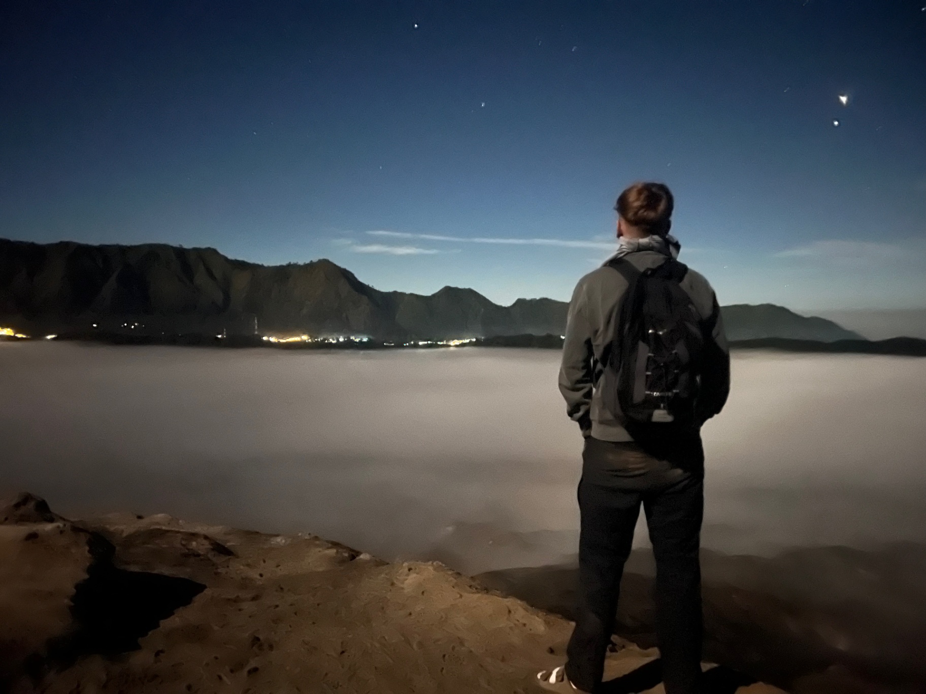 Mount Bromo — Above the clouds before sunrise, town lights still glowing below.