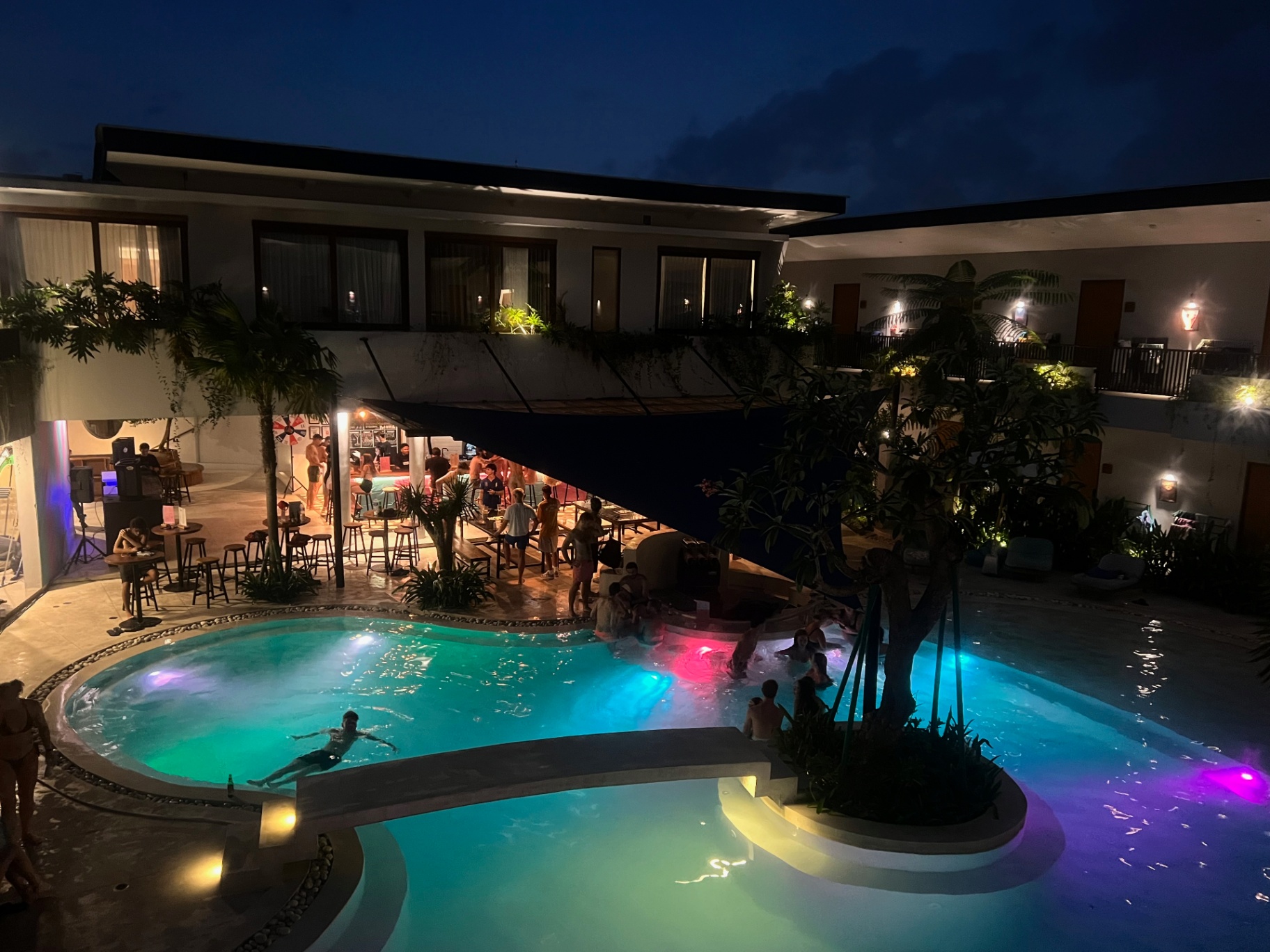 Bali — Hostel pool lit turquoise and pink as the night kicks off.