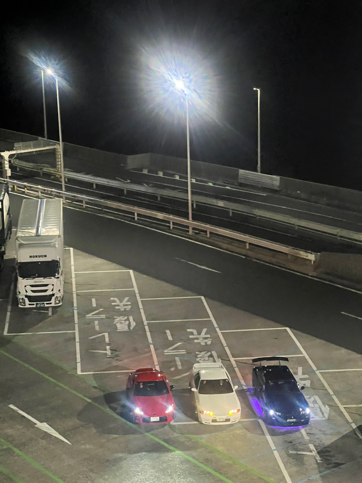 Tokyo — Three tuned cars lined up in a highway service area at midnight.