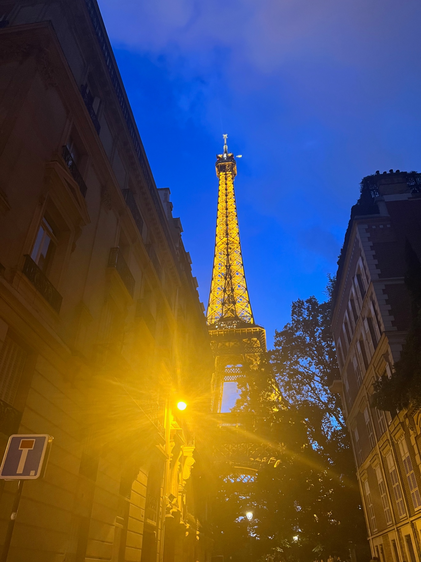 Paris — The Eiffel Tower lit gold at the end of a Haussmann street.