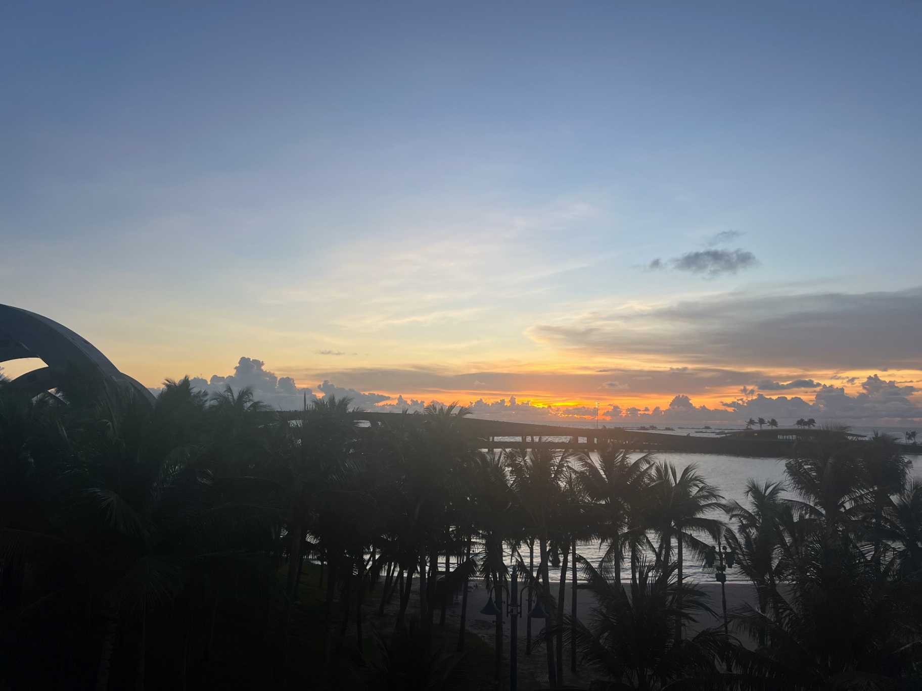 Phu Quoc — Sunset melting into the sea beyond the palms and resort roofs.