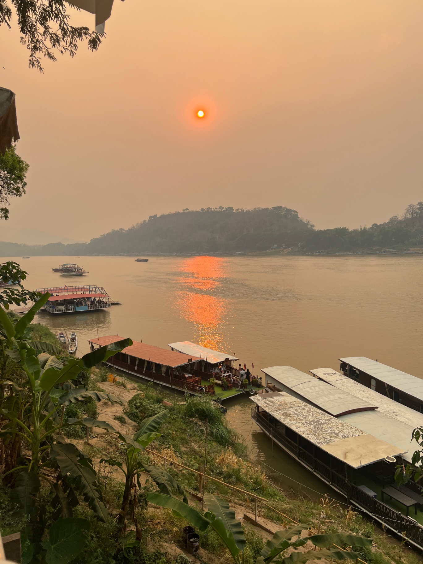 Luang Prabang — Hazy red sun setting over the Mekong river boats.