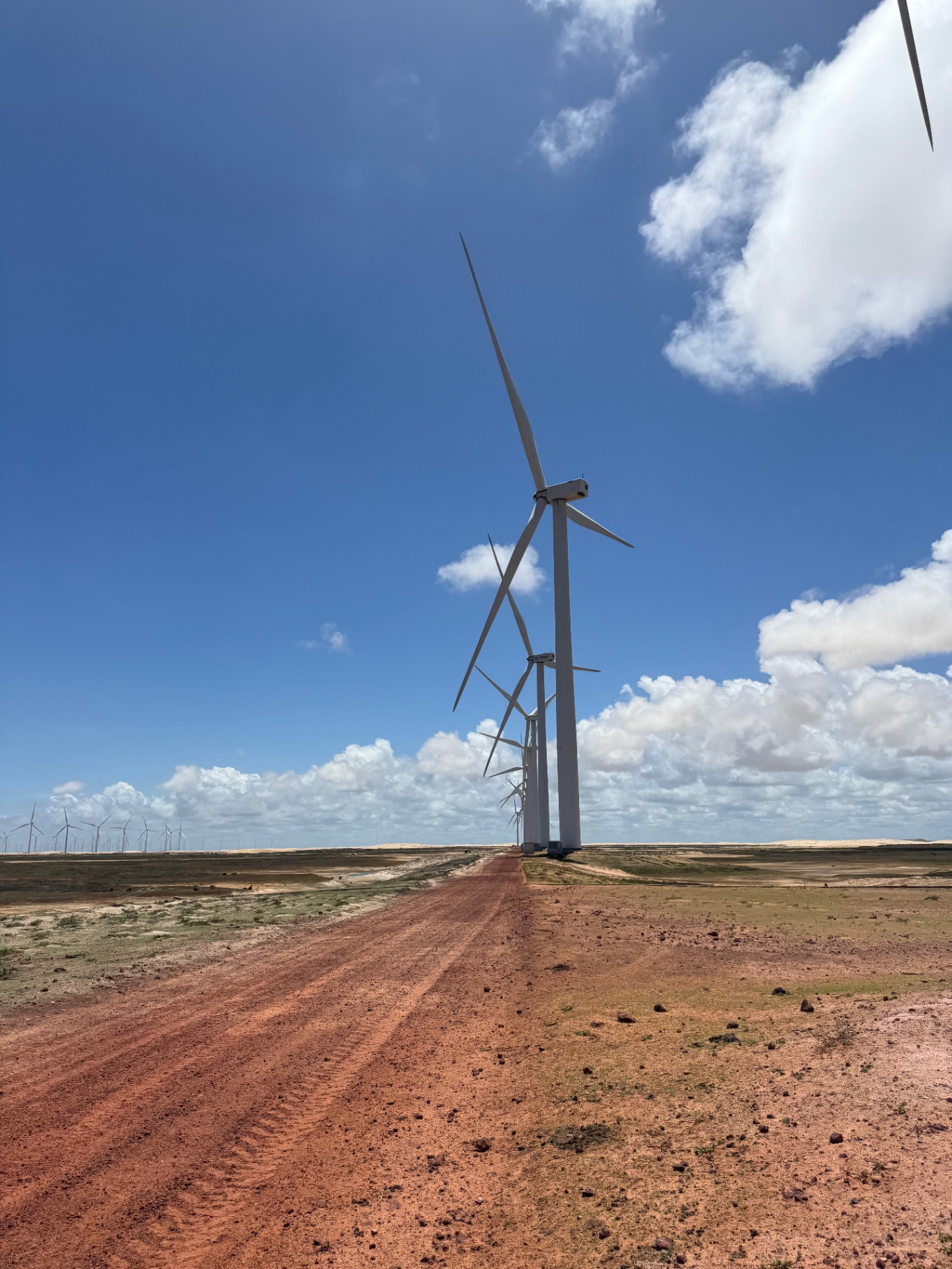 Lencois Maranhenses — Wind turbines rising beside the red-earth track.