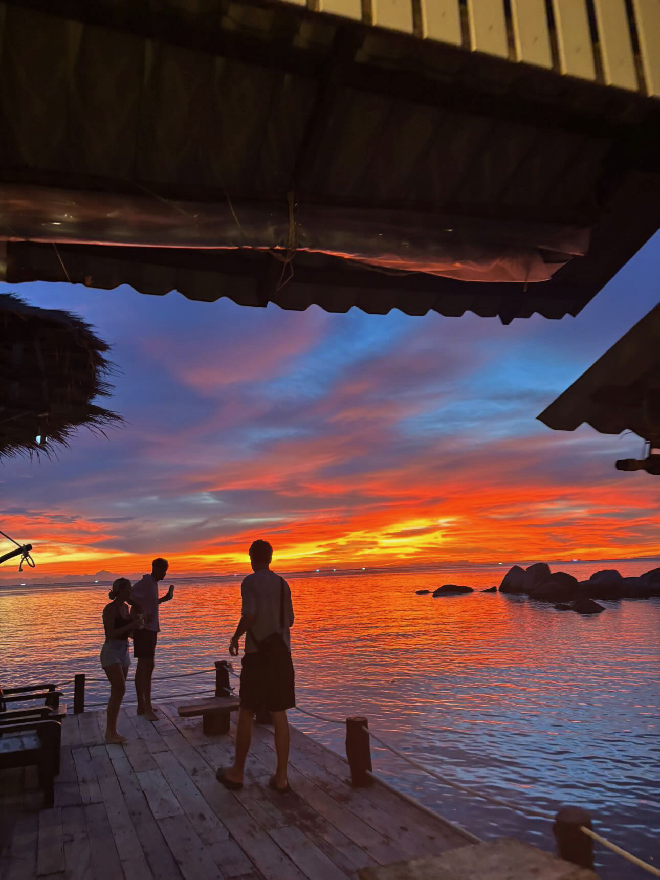 Ko Tao — Friends watching the sunset from a wooden dock bar.