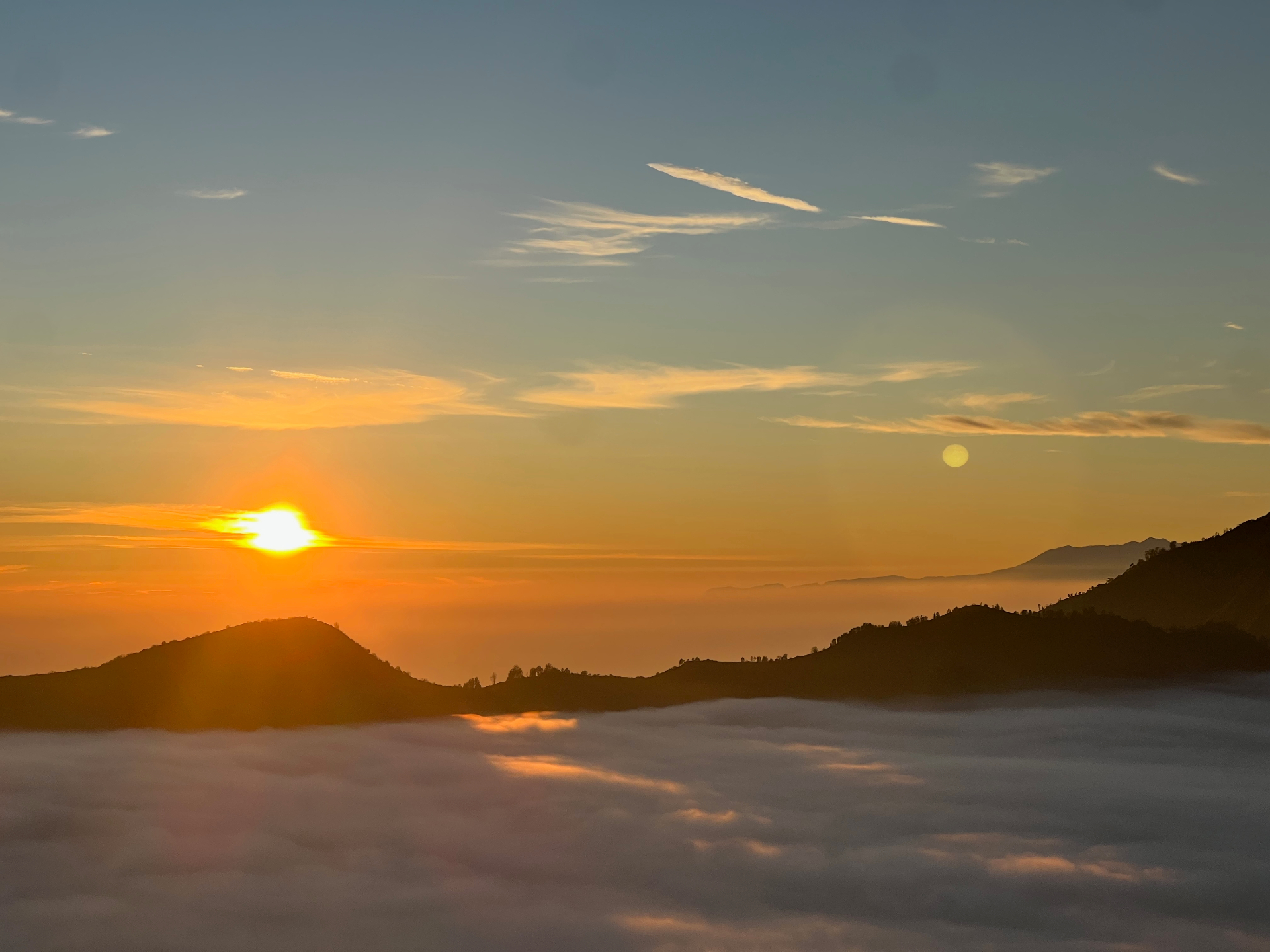 Mount Bromo — Sun and moon sharing the sky above a sea of clouds.
