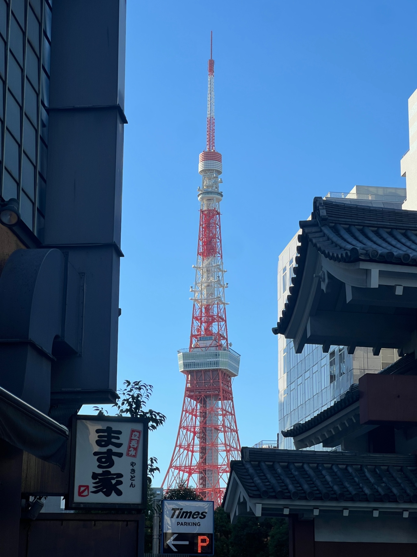 Tokyo — Tokyo Tower spearing a flawless blue sky, framed by tiled eaves and a kanji shop sign.