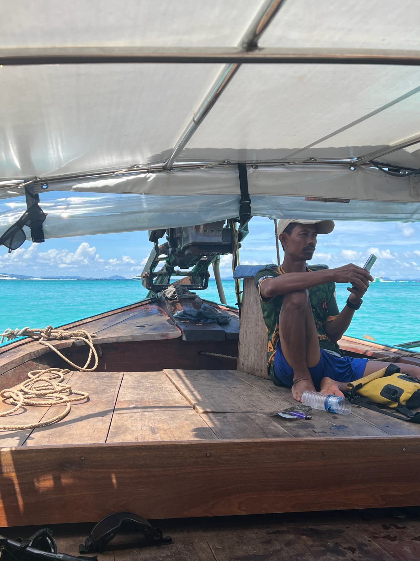 Phi Phi Island — Longtail boat captain checking his phone over turquoise water.